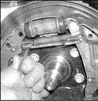 23. Подсоедините верхнюю возвратную пружину к передней тормозной колодке.